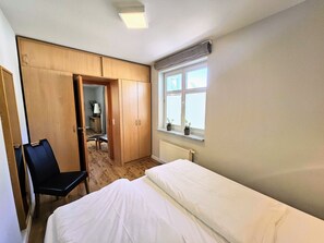 A bedroom with a bed, a chair, a wardrobe, and a window with blinds.