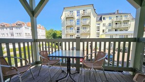 Een houten terras met een tafel en vier rieten stoelen, met uitzicht op een rij meerverdieping tellende gebouwen.