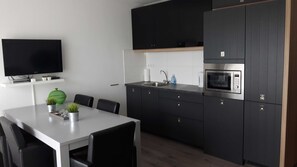 Ett modernt kök med mörka skåp, en inbyggd mikrovågsugn och en platt-TV som är monterad ovanför bänkskivan.