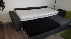 En praktisk bäddsoffa med madrass och ett svart fotstöd.