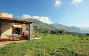 Ein Steingebäude mit Terrasse und Außenbestuhlung, mit Blick auf eine Berglandschaft und ein Gewässer.