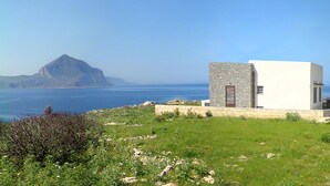 A coastal building with a stone facade, a small door, and a view of the sea and a mountain in the background. - Nice home in San Vito lo Capo -TP- with house sea view (San Vito lo Capo -TP-)