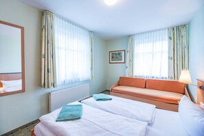Habitación de hotel con dos camas, un sofá, un radiador y cortinas.