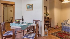 Ein Essbereich mit einem Tisch für vier Personen, Stühle mit karierten Kissen, einer Blumenvase und einem Gemälde an der Wand.