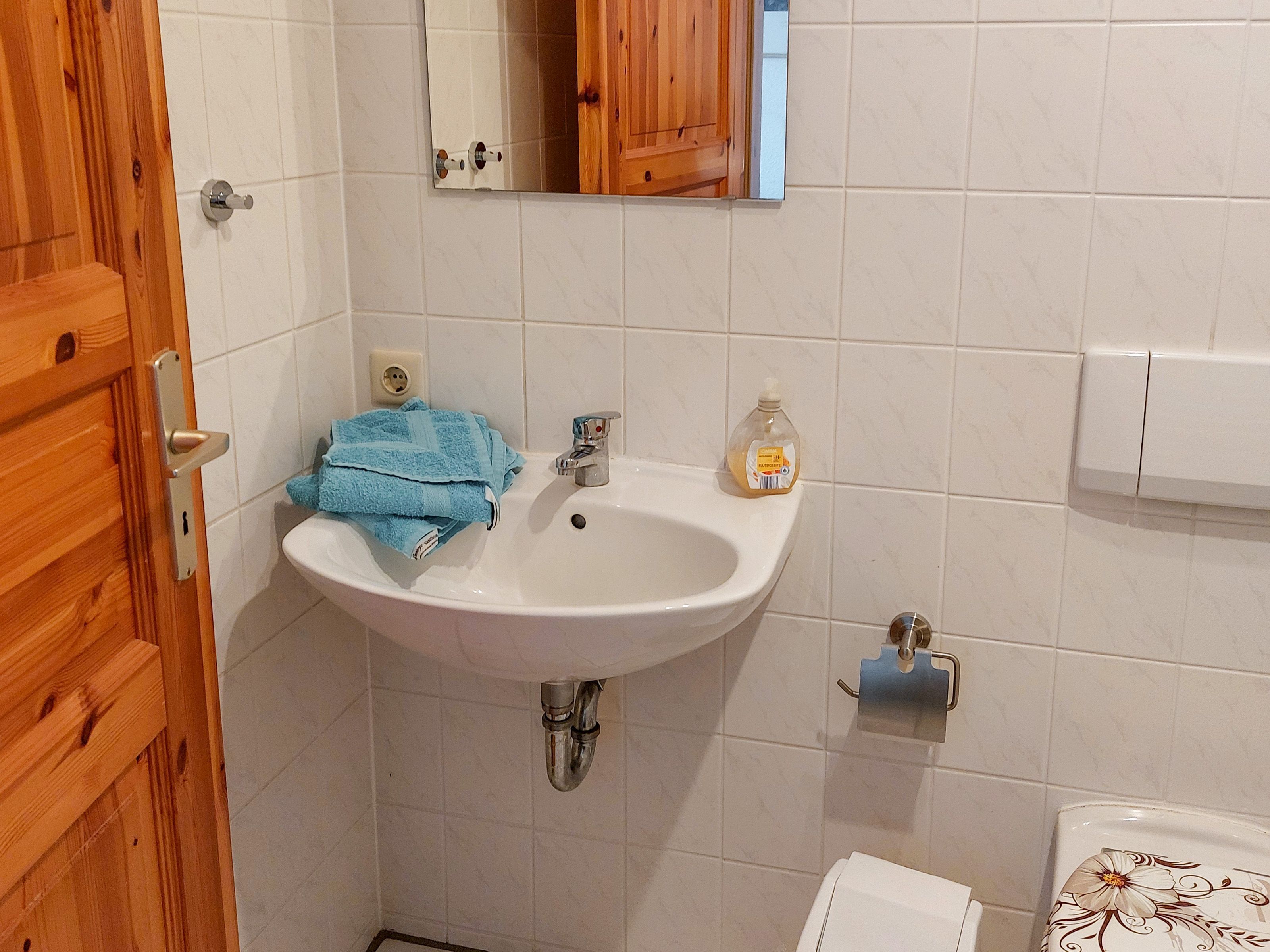 A bathroom with a white sink, a mirror, a wooden door, and a toilet.