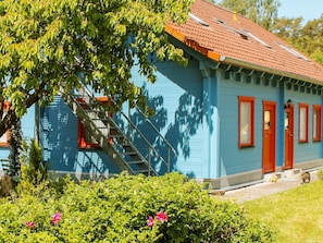 A blue house with a red roof, a visible staircase, and a small garden with pink flowers. - Double room 1 - Rankwitzer Hof (Rankwitz)