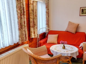 A cozy room with a red sofa, wicker chairs, a small round table with a vase, and floral curtains. - Double room 1 - Rankwitzer Hof (Rankwitz)