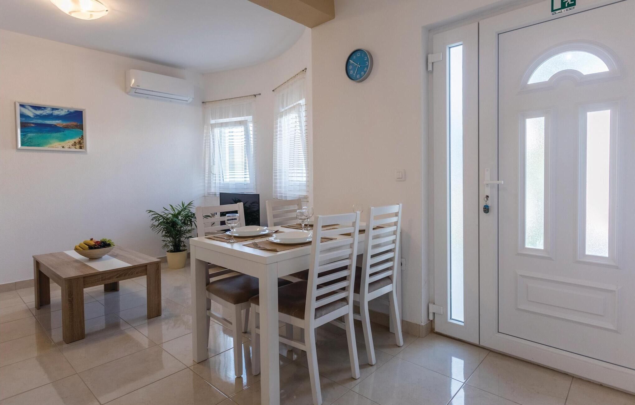 A dining area with a white table set for four, a potted plant, and a painting on the wall.