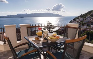 Una mesa con alimentos para el desayuno, vista al mar y un balcón con sillas.