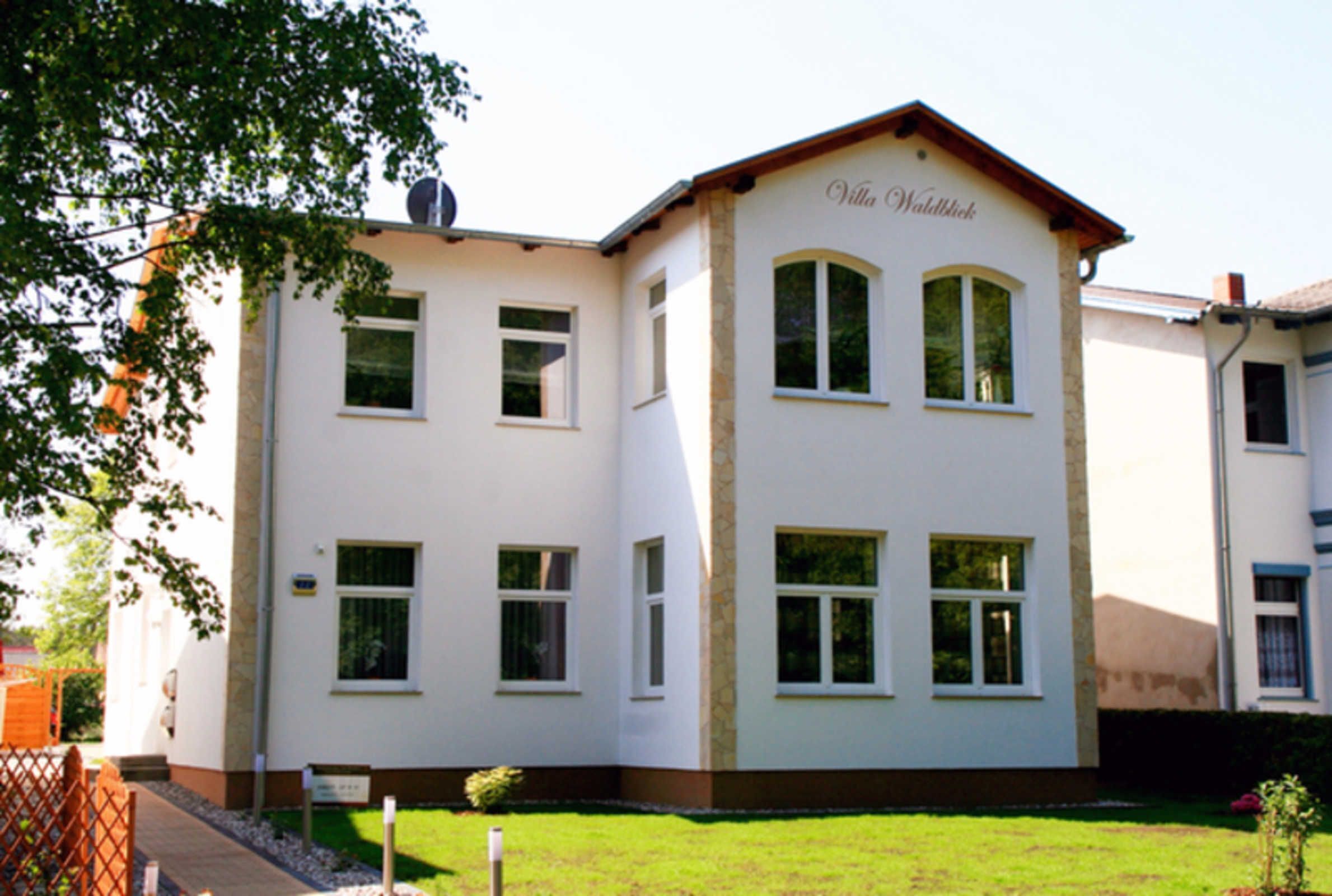 En tvåvåningsbyggnad med en vit fasad och ett brunt tak. Byggnaden har flera fönster och en skylt med texten ”Villa Waldwick”.