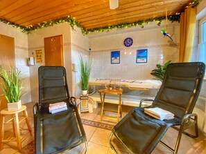 Une pièce avec deux chaises noires, une table en bois, une baignoire et une horloge au mur.