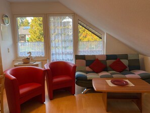 A room with a red sofa, two red chairs, a wooden table, and a window with lace curtains. - Apartment 4 Marguerite - House Jasmine (Sankt Andreasberg)