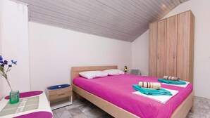 Une chambre à coucher comprenant un lit, une table de chevet, une armoire et une petite table sur laquelle est posé un vase de fleurs.