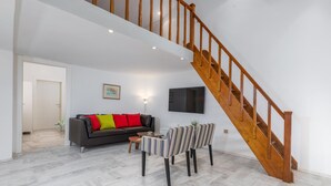 Een woonkamer met een bank, stoelen, een televisie en een houten trap.
