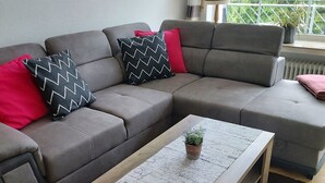 Een moderne woonkamer met een grijze modulaire bank, een houten salontafel en een kamerkleed met een patroon.