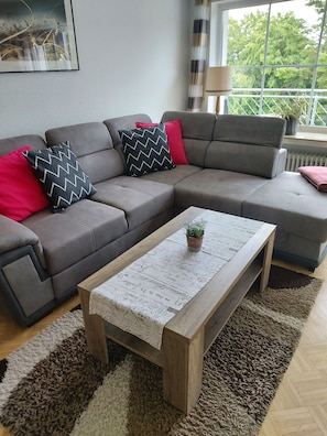 Un salon moderne avec un canapé d’angle gris, une table basse en bois et un tapis à motifs.