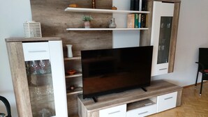 A modern living room with a flat-screen TV on a wooden stand, white cabinets with glass doors, and a wooden herringbone floor. - Apartment Debray 2 ****, 78 sqm - Apartments Debray **** (Winterberg)
