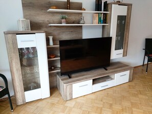 A modern living room with a flat-screen TV on a wooden stand, white cabinets with glass doors, and a wooden herringbone floor.