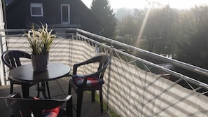 A balcony with a table and chairs, a potted plant, and a view of a house and trees.