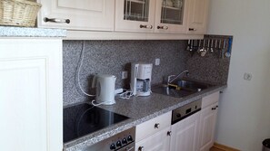A kitchen with white cabinets, a granite countertop, a coffee maker, a kettle, a sink, and a dish rack.