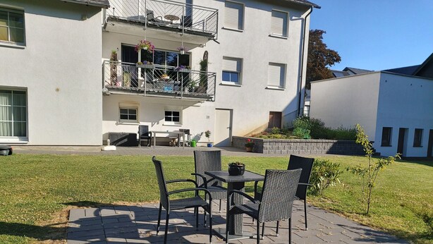 A two-story building with a balcony, outdoor seating, and a wheelbarrow. - Apartment Debray 2 ****, 78 sqm - Apartments Debray **** (Winterberg)