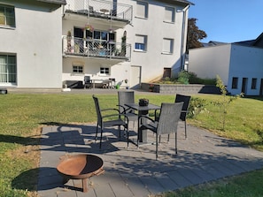 A two-story building with a balcony, outdoor seating, and a wheelbarrow.