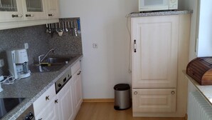 Een keuken met een granieten aanrechtblad, witte kastjes, een magnetron en een prullenbak.