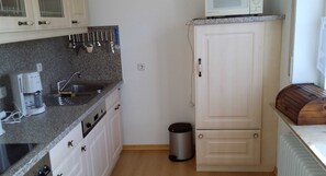 Une cuisine dotée d’un plan de travail en granit, de meubles blancs, d’un four à micro-ondes et d’une poubelle.