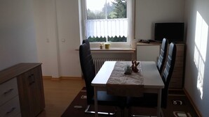 A dining area with a table, chairs, a radiator, a window with curtains, a television, and a cabinet. - Apartment Debray 2 ****, 78 sqm - Apartments Debray **** (Winterberg)