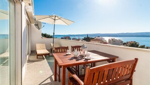 Un balcone con un tavolo e sedie in legno, un ombrellone bianco e vista sul mare e sugli edifici.