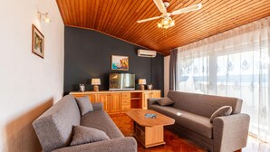 Un soggiorno moderno con soffitto in legno, un'ampia finestra con tende, un divano, un tavolino da caffè e una TV su un mobile in legno.
