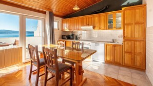 Una cucina moderna con mobili in legno, un tavolo da pranzo in vetro e vista sul mare.