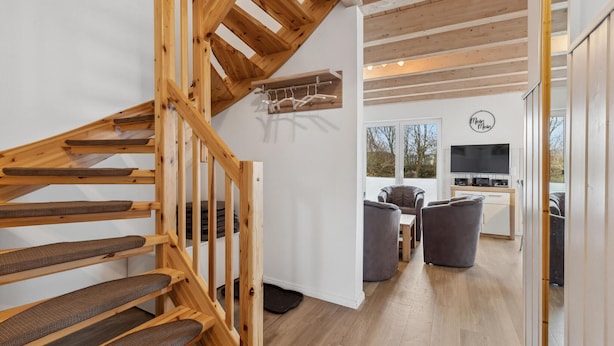 Un intérieur moderne avec un escalier en bois, un coin repas doté de meubles gris et une cuisine équipée d’un téléviseur.