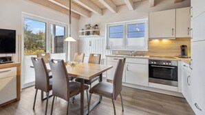 Une cuisine moderne avec des meubles blancs, un four Bosch et un coin repas comprenant une table en bois et des chaises en cuir.