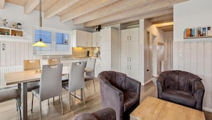 Une cuisine moderne avec des meubles blancs, un plafond en bois et un coin repas comprenant une table et des chaises.