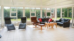 A spacious living room with large windows, a black leather sofa, a brown leather armchair, and a reclining chair. - 4 bedroom amazing home in Ribe (Ribe)