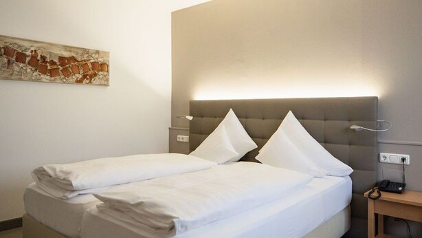 Habitación de hotel con cama doble, mesita de noche con lámpara y una obra de arte colgada en la pared.