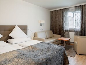 Una habitación de hotel con cama, sofá, una mesita y ventana con cortinas.