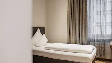 Una cama bien hecha con sábanas blancas, cabecero oscuro y una ventana con cortinas translúcidas.