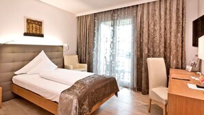 Una habitación de hotel con cama, escritorio, silla y ventana con cortinas.