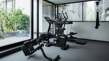Ein Fitnessstudio mit Trainingsgeräten, großen Fenstern und Blick auf Grünflächen.