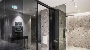 Un baño moderno con cabina de ducha de vidrio, paredes de mármol y un secamanos visible.