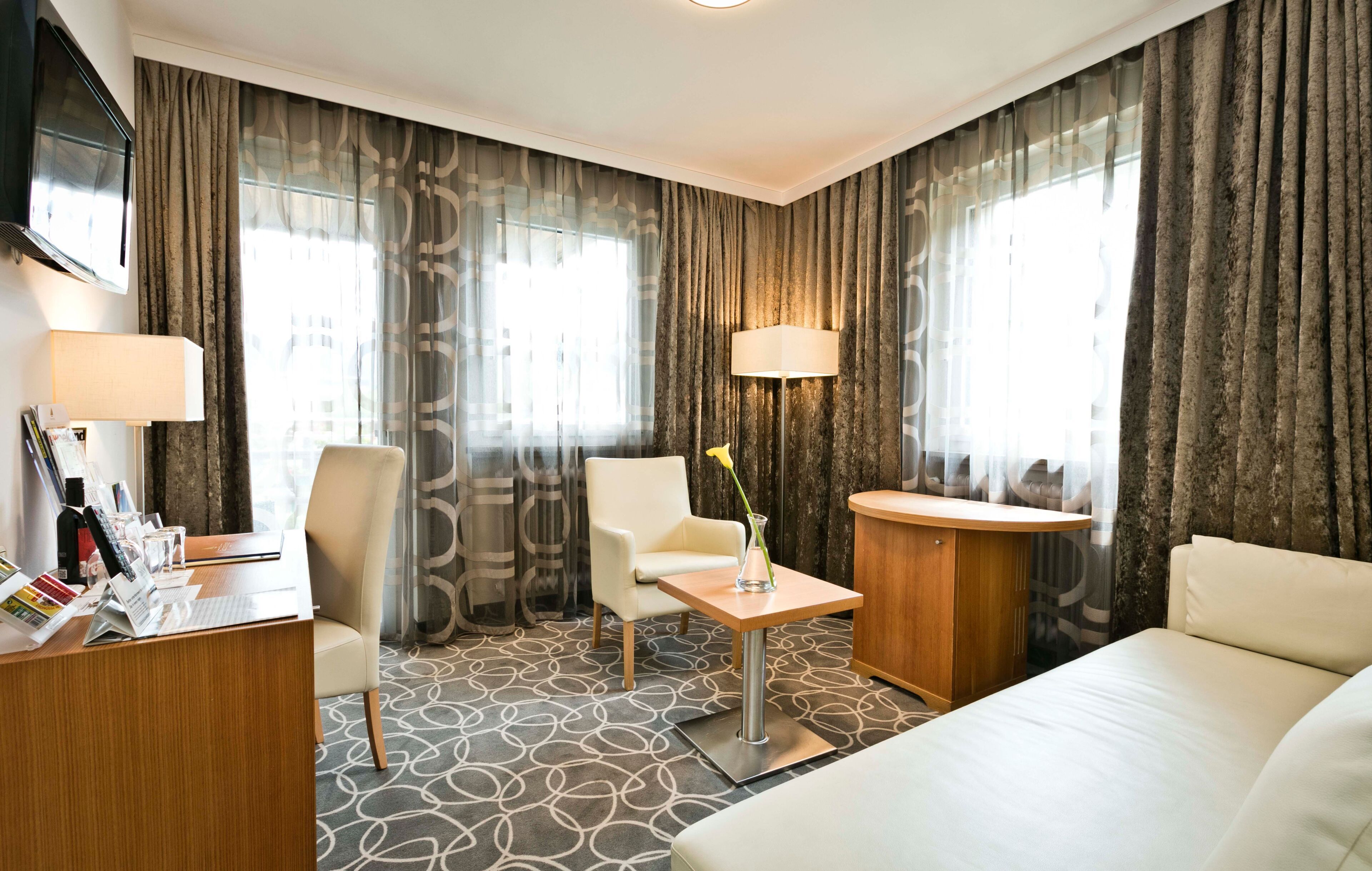 Une chambre d’hôtel comprenant un lit, un bureau, une chaise, une petite table avec un vase et deux lampes.