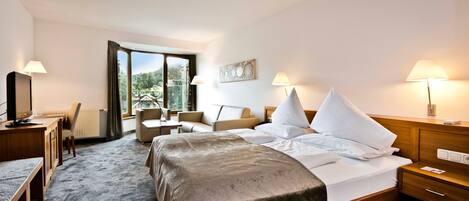 A hotel room with a bed, bedside tables, a desk, a chair, and a view of the outdoors.