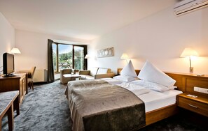 A hotel room with a bed, bedside tables, a desk, a chair, and a view of the outdoors.