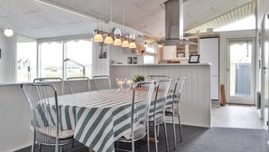 Une cuisine moderne dotée d’un îlot central, de luminaires suspendus et d’un coin repas avec des nappes à rayures et des chaises en métal.