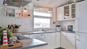 Une cuisine moderne avec des armoires blanches, un comptoir en granit, un four encastré et une fenêtre donnant sur un paysage verdoyant.