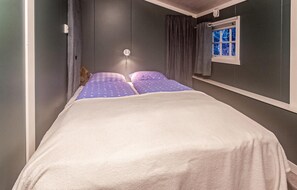 A narrow room with a bed, a window with curtains, and a wall-mounted light. - 3 bedroom nice home in Leknes (Leknes)