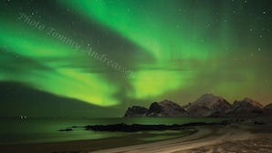 Una playa con una cadena montañosa al fondo bajo una exhibición de aurora verde.