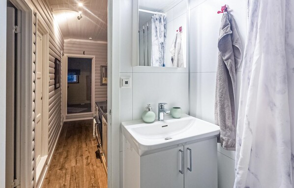 Baño con lavamanos blanco, dos dispensadores de jabón verdes, un espejo y una cortina de ducha.